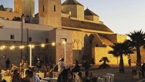 Un edificio histórico con dos torres destacadas y un patio donde hay gente reunida.