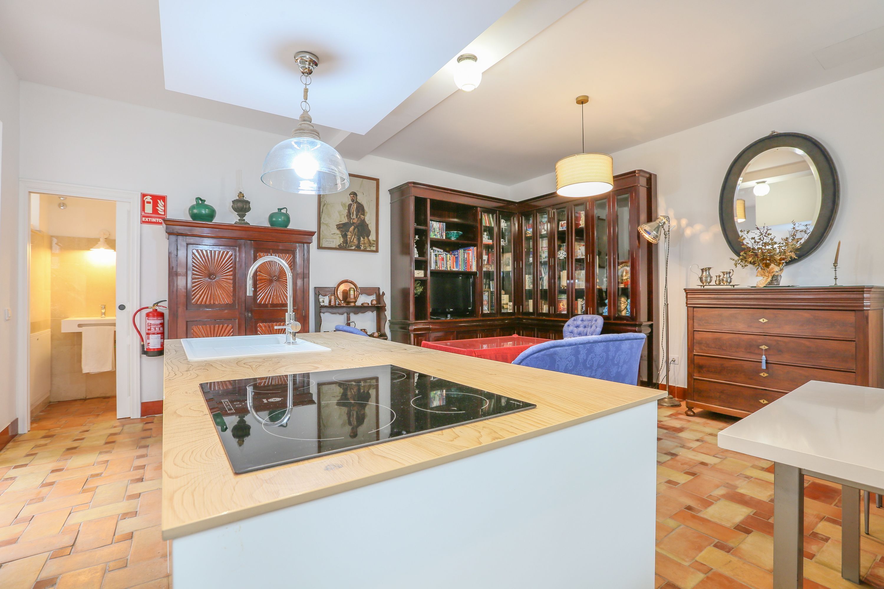 A kitchen with a central island, wooden cabinets, a bookshelf, and a dining area with a table and chairs.