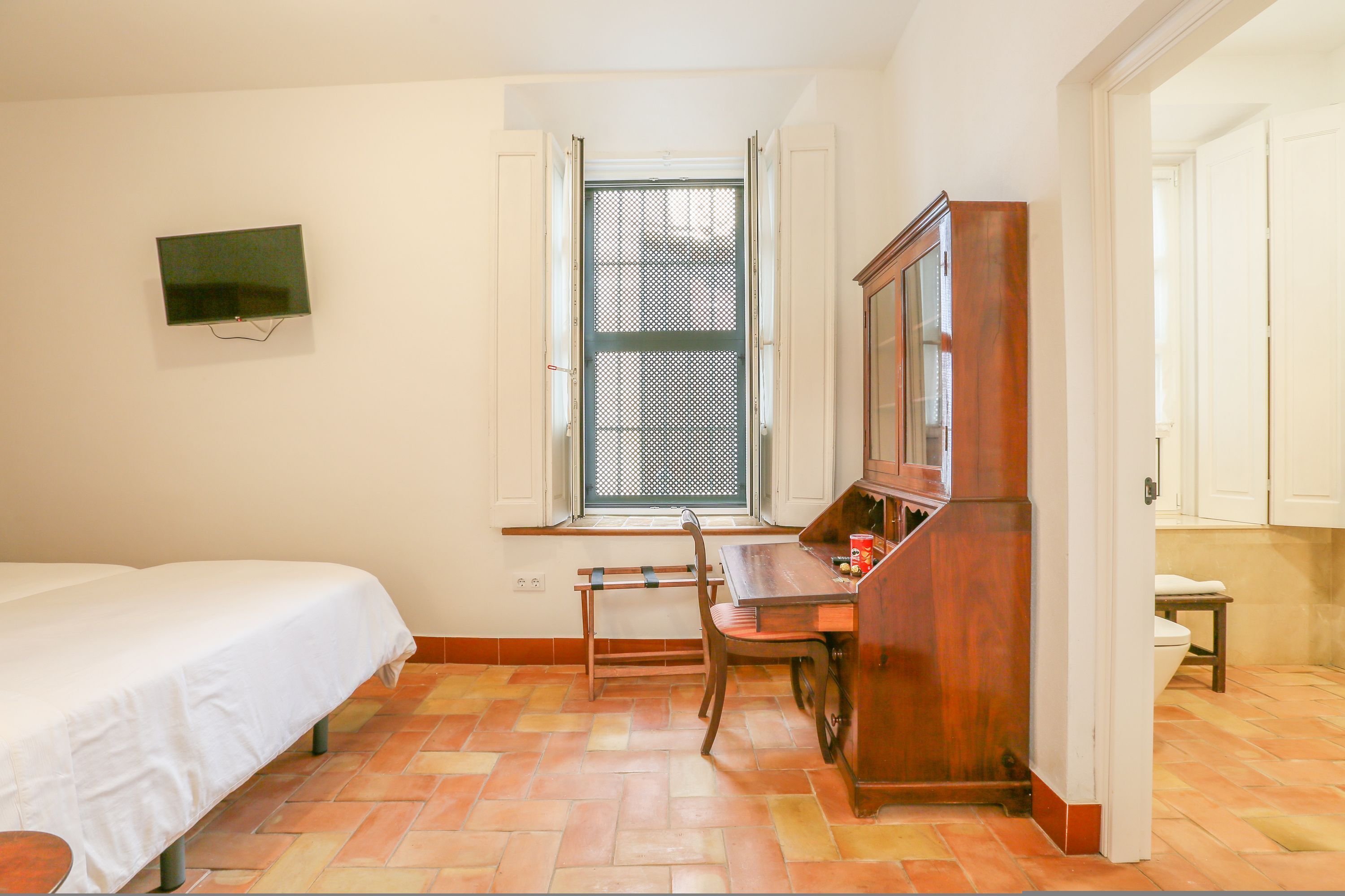 A room with a bed, a desk, a chair, a television, and a window with a view.