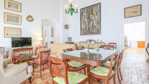 A dining area with a large table and chairs, a television, and a painting on the wall. - Posada De La Casa Del Pintor Hab C diz (Carmona)