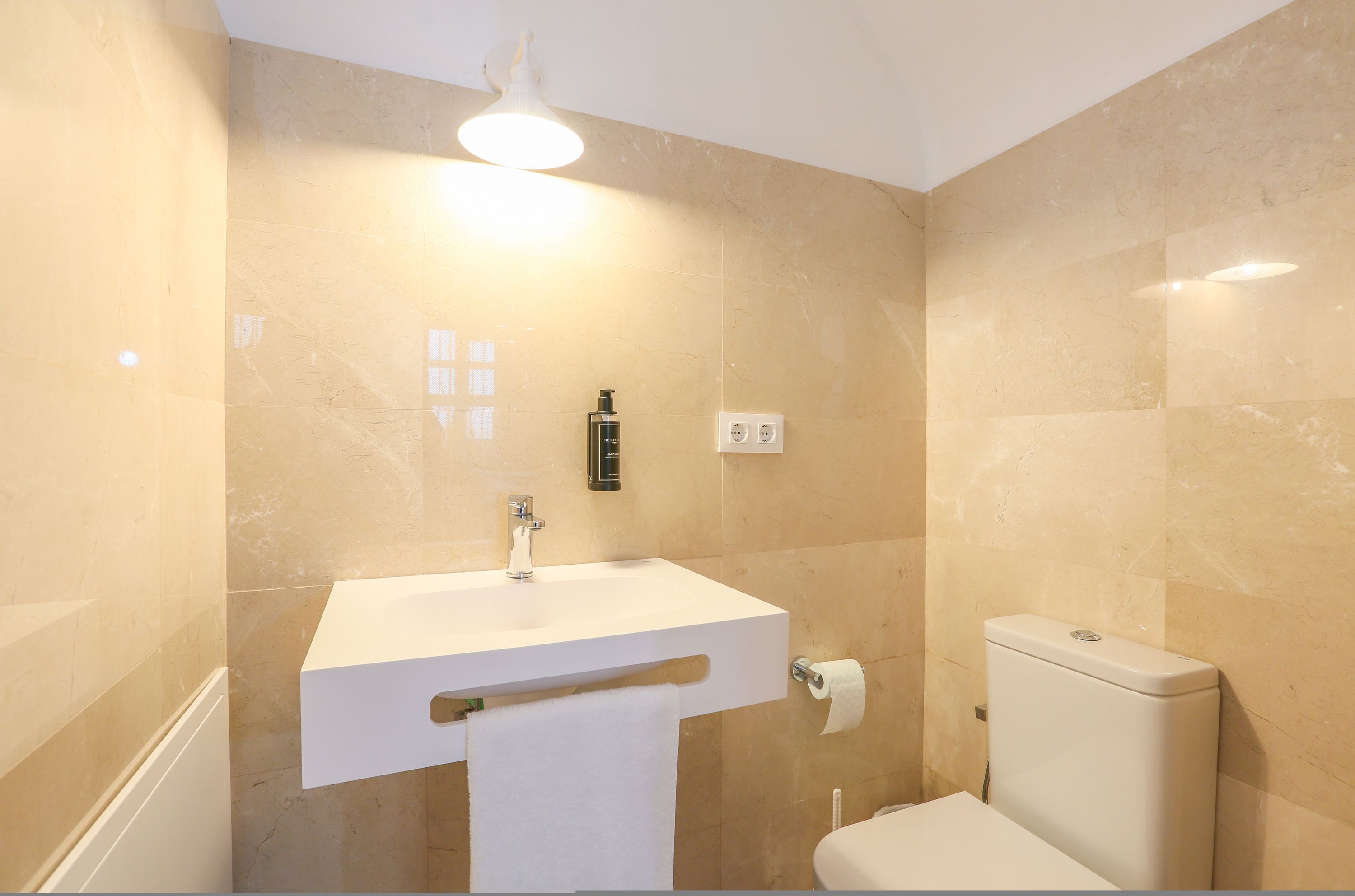 Ein Badezimmer mit einem weißen Waschbecken, einer Toilette und einem Handtuch an der Wand.
