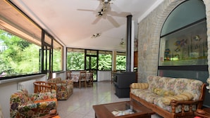 A spacious living room with a fireplace, large windows, and a stone wall. - Villa Francesca in Scheggia (Anghiari)
