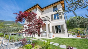 A two-story house with a balcony, a garden with stepping stones, and a clear blue sky. - Ricomilla Holiday-finestra Sul Verde- (Roe Volciano)
