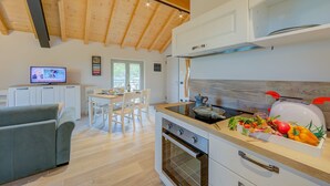 A modern kitchen with wooden beams, a dining area with a white table and chairs, and a television in the background. - Ricomilla Holiday-finestra Sul Verde- (Roe Volciano)