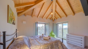 A bedroom with a wooden ceiling, a bed with a patterned bedspread, two windows, and a white dresser. - Ricomilla Holiday-finestra Sul Verde- (Roe Volciano)