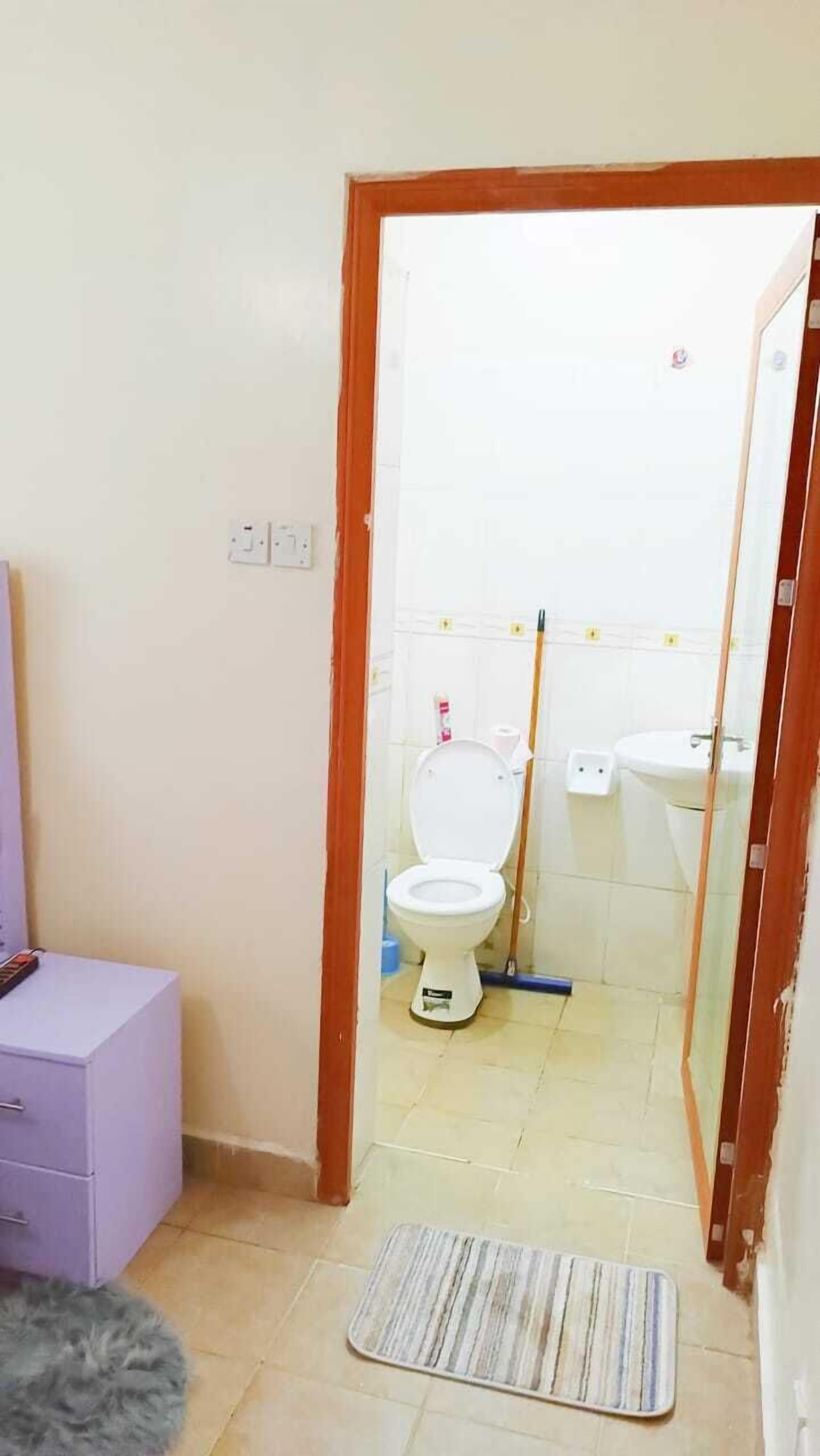 Et badeværelse med toilet, bidet og vask. Der er et spejl, en moppe og en måtte på gulvet.