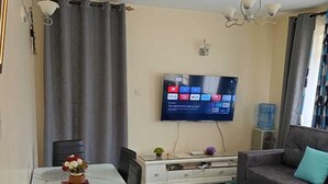Un saló amb zona de menjador, un sofà, un televisor fixat a la paret i un dispensador d'aigua.