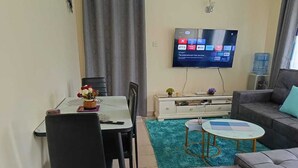 Un saló amb un televisor penjat a la paret, una taula de dinar amb cadires, un sofà i una taula de centre.