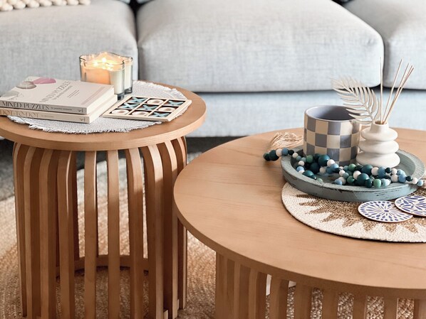 A cozy living room with a round wooden coffee table, a side table, and a lit candle.
