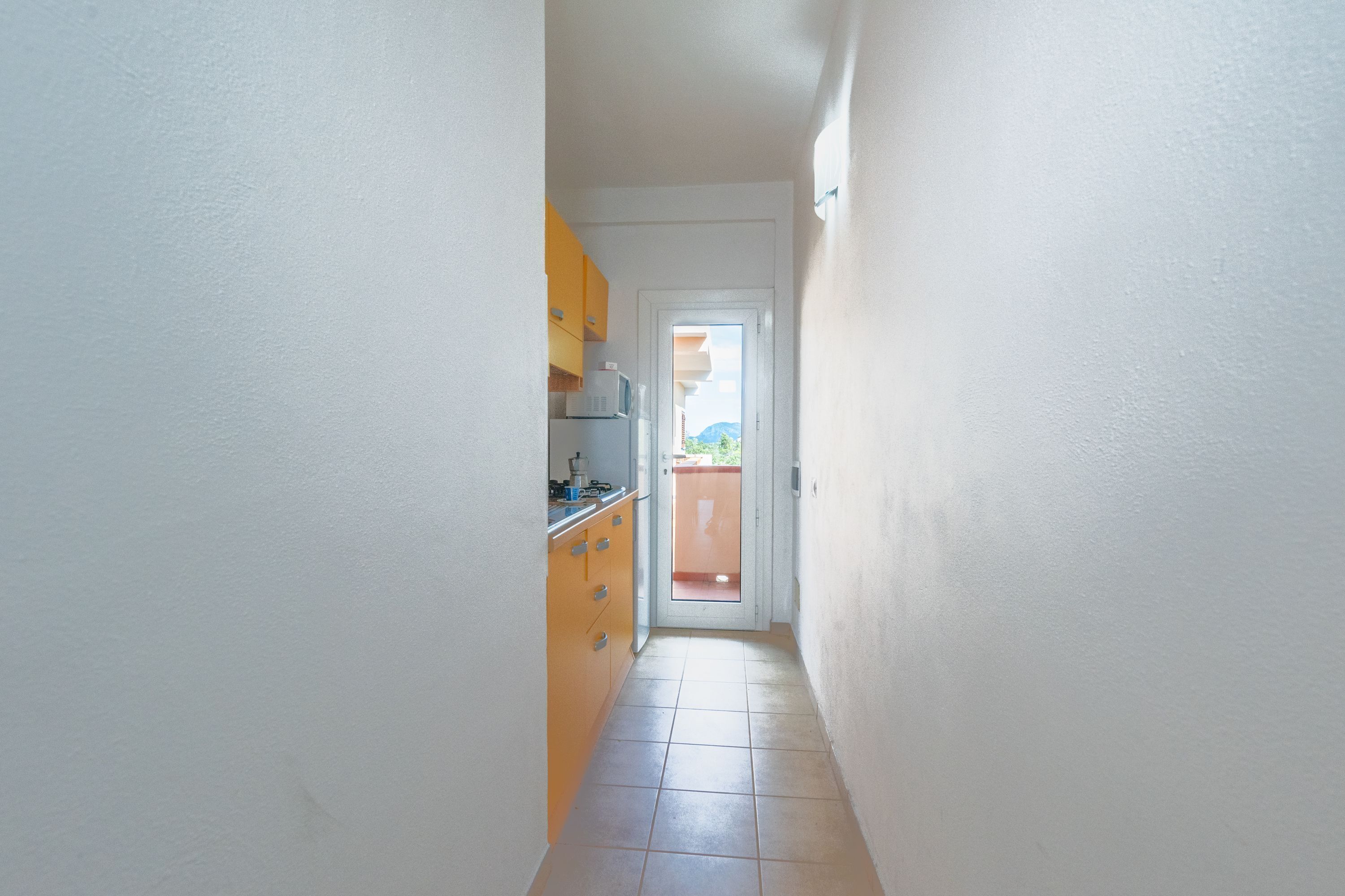 A narrow hallway with a kitchen area on the left, featuring yellow cabinets and a microwave.