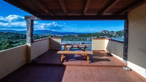 A wooden deck with a picnic table and a stone pillar, overlooking a mountainous landscape. - Monte Majore 16 B in Porto Rotondo (Olbia)