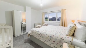 Une chambre à coucher avec un lit, un berceau, une armoire et une fenêtre avec des rideaux.