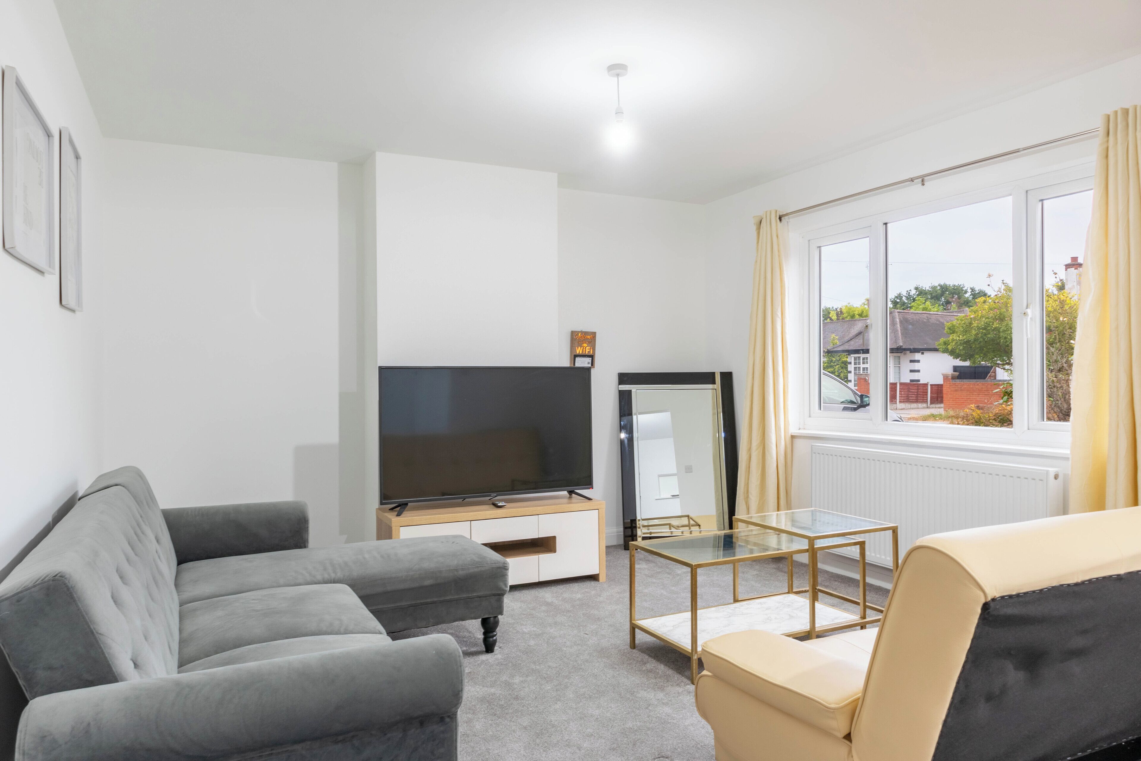 A modern living room with a grey sofa, a beige sofa, a glass coffee table, and a flat-screen TV on a wooden stand.