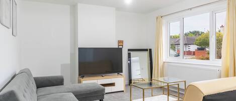 A modern living room with a grey sofa, a beige sofa, a glass coffee table, and a flat-screen TV on a wooden stand.