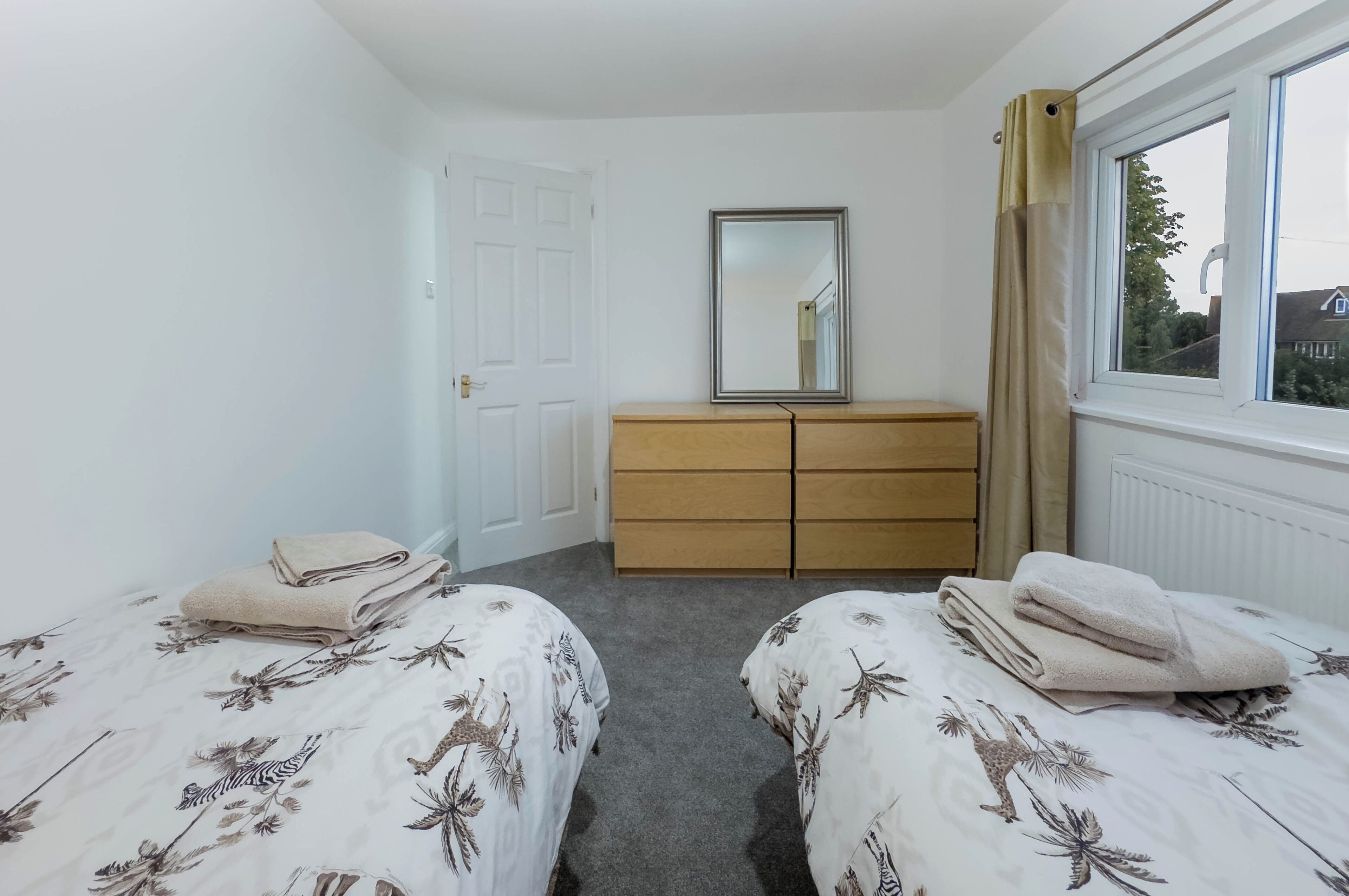 A bedroom with two beds, a dresser, a mirror, and a window with a view of the outside.