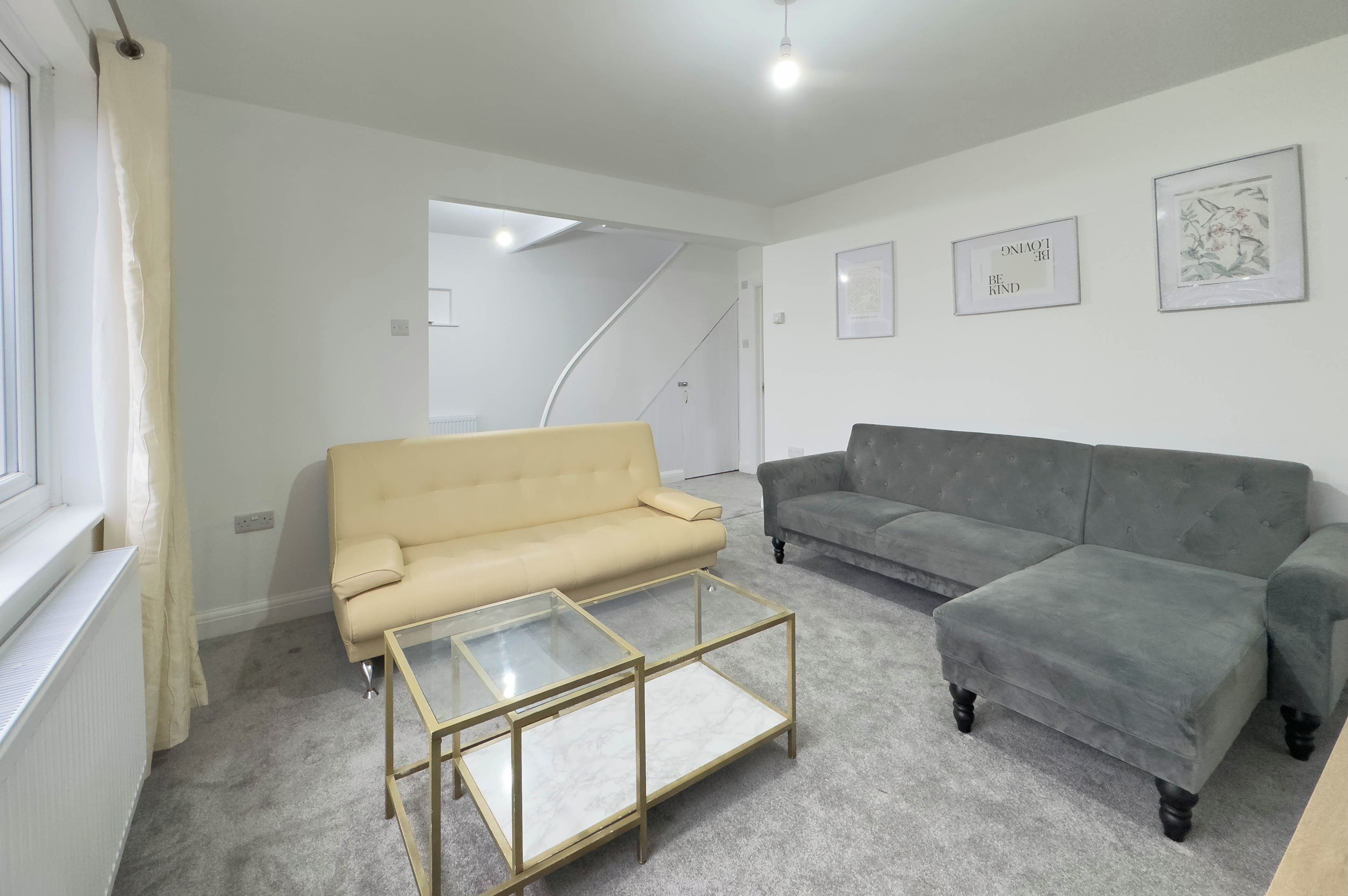 A living room with two sofas, a glass coffee table, and a staircase leading to another room.