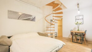 A bedroom with a large bed, a wooden spiral staircase, a dining area with a table and chairs, and a wall-mounted picture. - Villa Claudia in Sevilla (Seville)