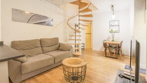 A modern living room with a spiral staircase, a sofa, a round coffee table, and a dining area with chairs and a table. - Villa Claudia in Sevilla (Seville)