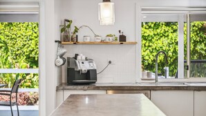 Een moderne keuken met een koffieapparaat, een plank met planten en een raam met uitzicht op groen.