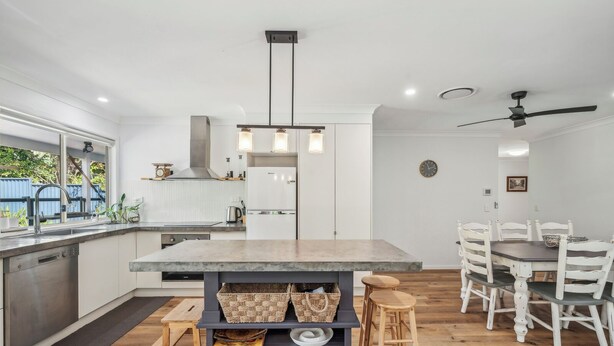 Een moderne keuken met een centraal eiland, houten krukken en een eethoek met witte stoelen.