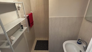 A small bathroom with a white sink, a red towel, and a shower area.