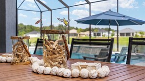 Une table ornée d’objets décoratifs, notamment un bocal en verre contenant du bois flotté et une décoration représentant un insecte suspendue, le tout placé devant un espace extérieur abrité, avec des chaises et une vue sur une piscine.