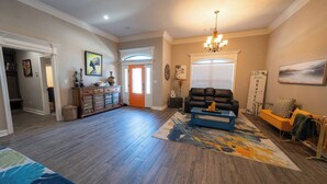 A spacious living room with hardwood flooring, a blue coffee table, a black leather sofa, and a colorful rug. - Veteran’s Family Retreat, Spacious & Peaceful Stay Near AFB (Sherwood)