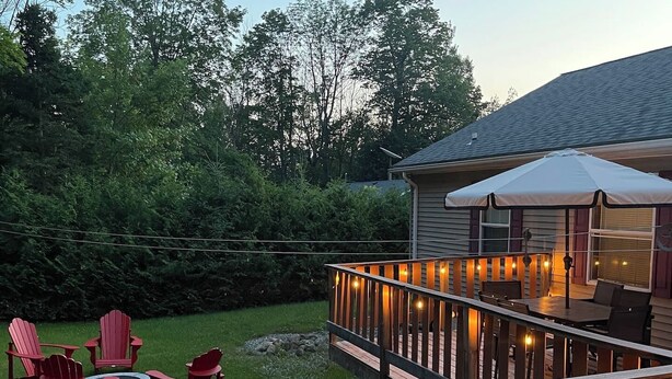 A wooden deck with a railing, outdoor seating with chairs, and a covered area with tables and chairs. - Maple Cottage at Miller Lake: Your Serene Nature Escape (Miller Lake)