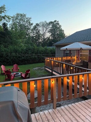 Een houten terras met een leuning, buitenmeubels met stoelen, en een overdekt gedeelte met tafels en stoelen.