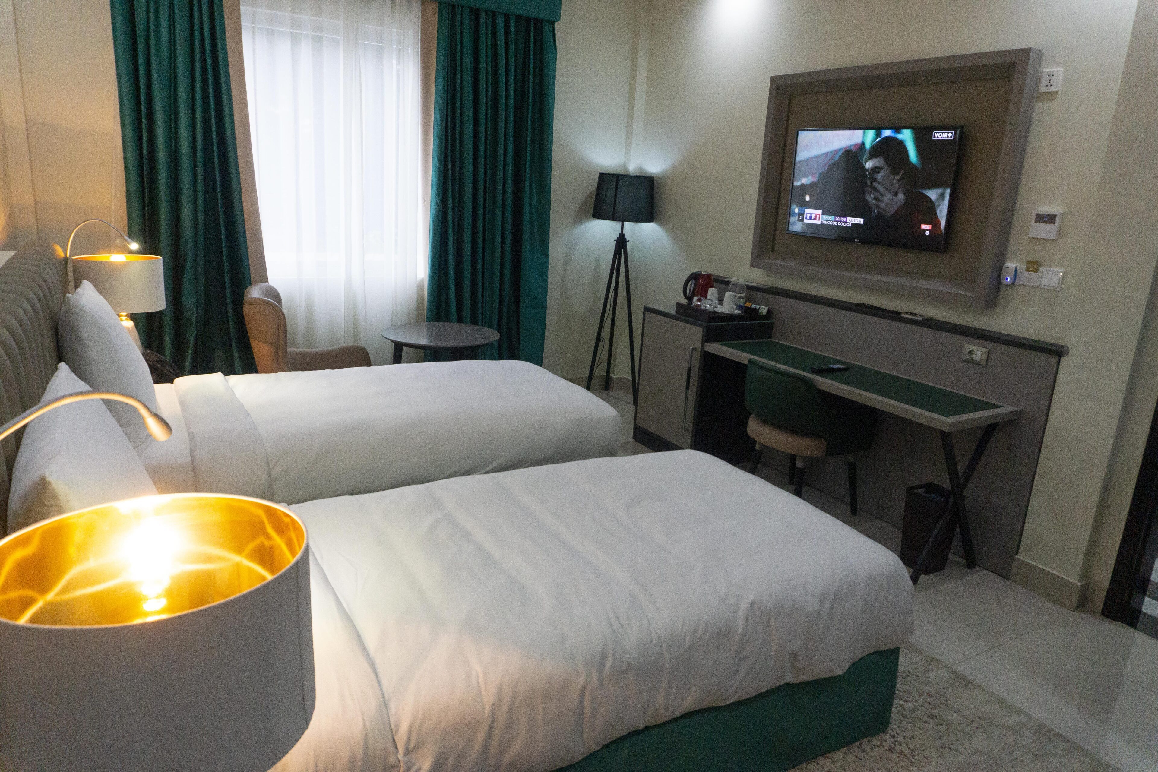 A hotel room with two beds, a desk, a television, a lamp, and a view of the outdoors.