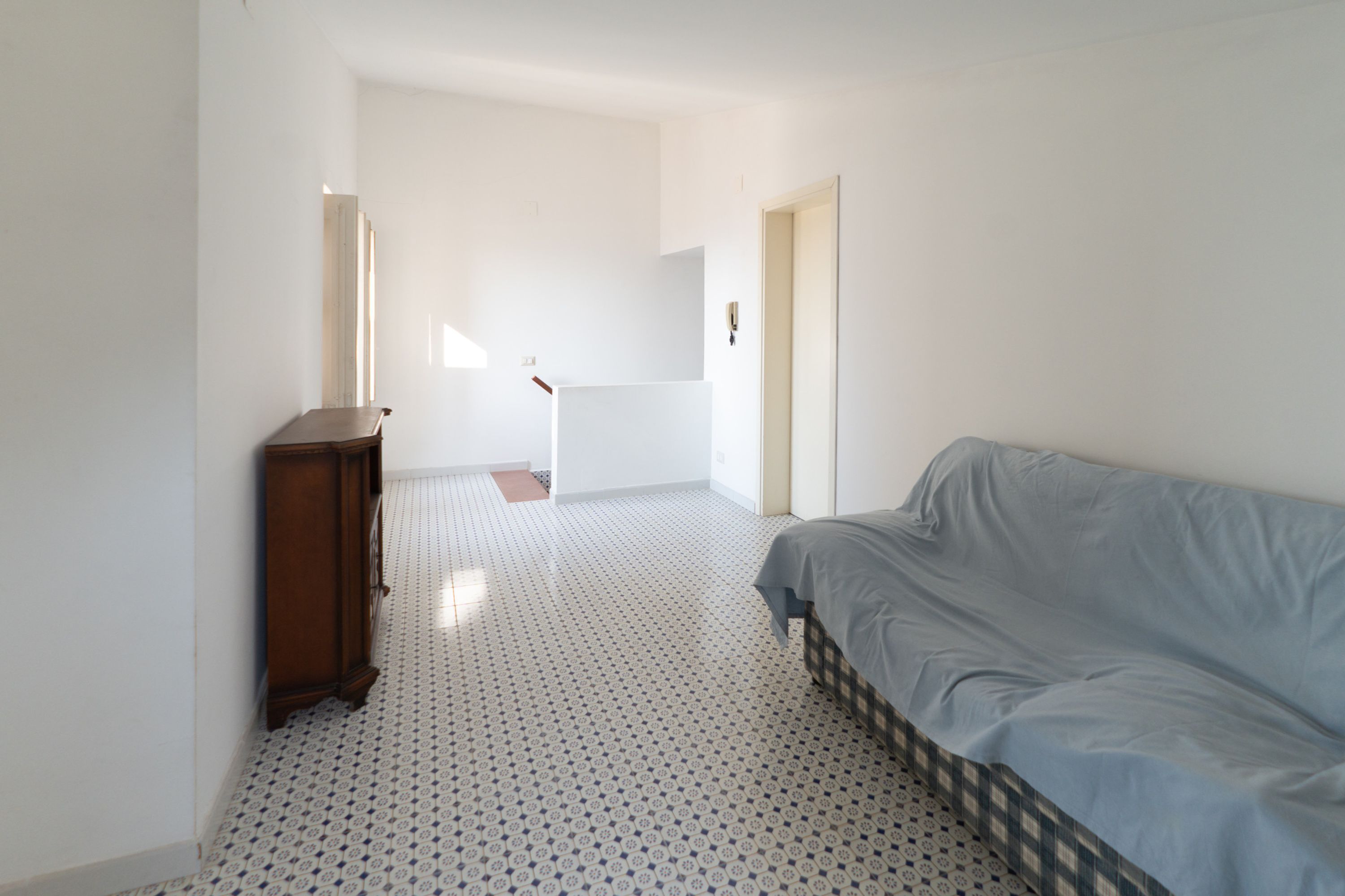 A room with a bed, a wooden dresser, and a patterned floor.