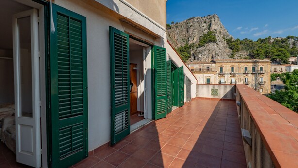 Un balcon avec des volets verts, un sol carrelé et une vue sur une montagne.