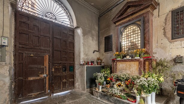 An interior with a large wooden door, a marble altar with flowers, and a stone floor. - Ale Cozy House by Wonderful Italy (Palermo)