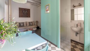 A room with a checkered floor, a sofa, a table with a vase of flowers, a painting on the wall, and a bathroom with a sink and mirror. - Ale Cozy House by Wonderful Italy (Palermo)
