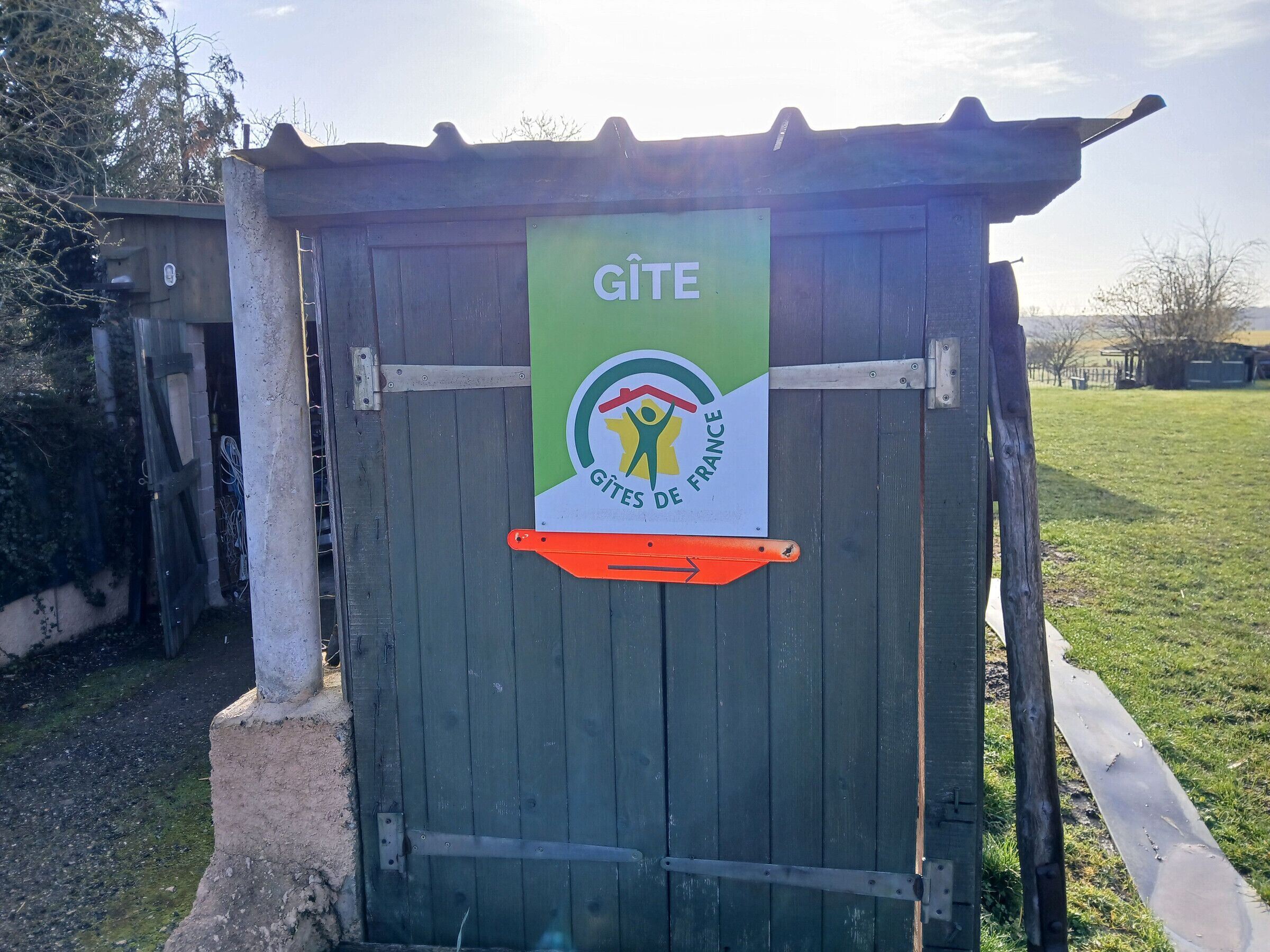 Een houten gebouw met een bord waarop 'GÎTE GÎTES DE FRANCE' staat en een logo van een persoon met een vlag.