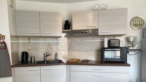 Eine moderne Küche mit hellen Holzschränken, einer Edelstahl-Spüle, einer Kaffeemaschine, einem Toaster und einem Mülleimer.