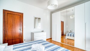 A bedroom with a wooden door, a white dresser, a bed with a striped bedspread, and a large mirror reflecting the room. - GuestHost - 90 sqm apartment for 4 people in Perugia, with a balcony and unassigned on-site parking. Located just a 10-minute walk from the historic center, it offers tranquility without sacrificing convenience. Perugia, renowned for its rich medieval hi (Perugia)