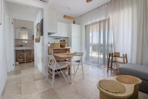 A modern kitchen with white cabinets, a wooden table, and a grey sofa.