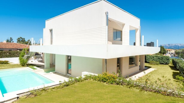 A modern two-story house with a swimming pool, large windows, and a view of the mountains.