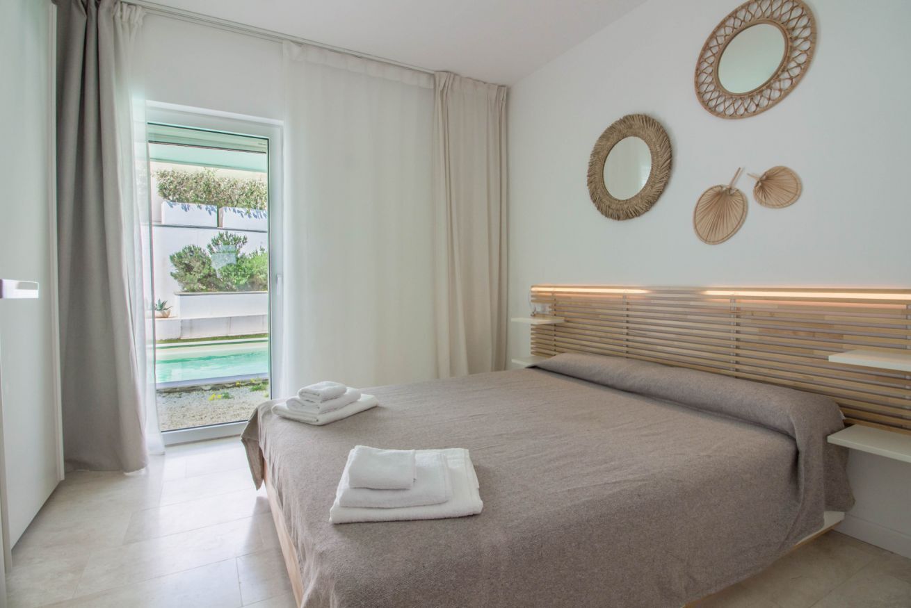 A bedroom with a bed, a window with curtains, and wall-mounted mirrors.