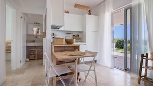 A modern kitchen with white cabinets, a wooden dining table, and a view through a glass door.