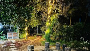 Een tuin met een pad van stenen, houten palen en lichtslingers.