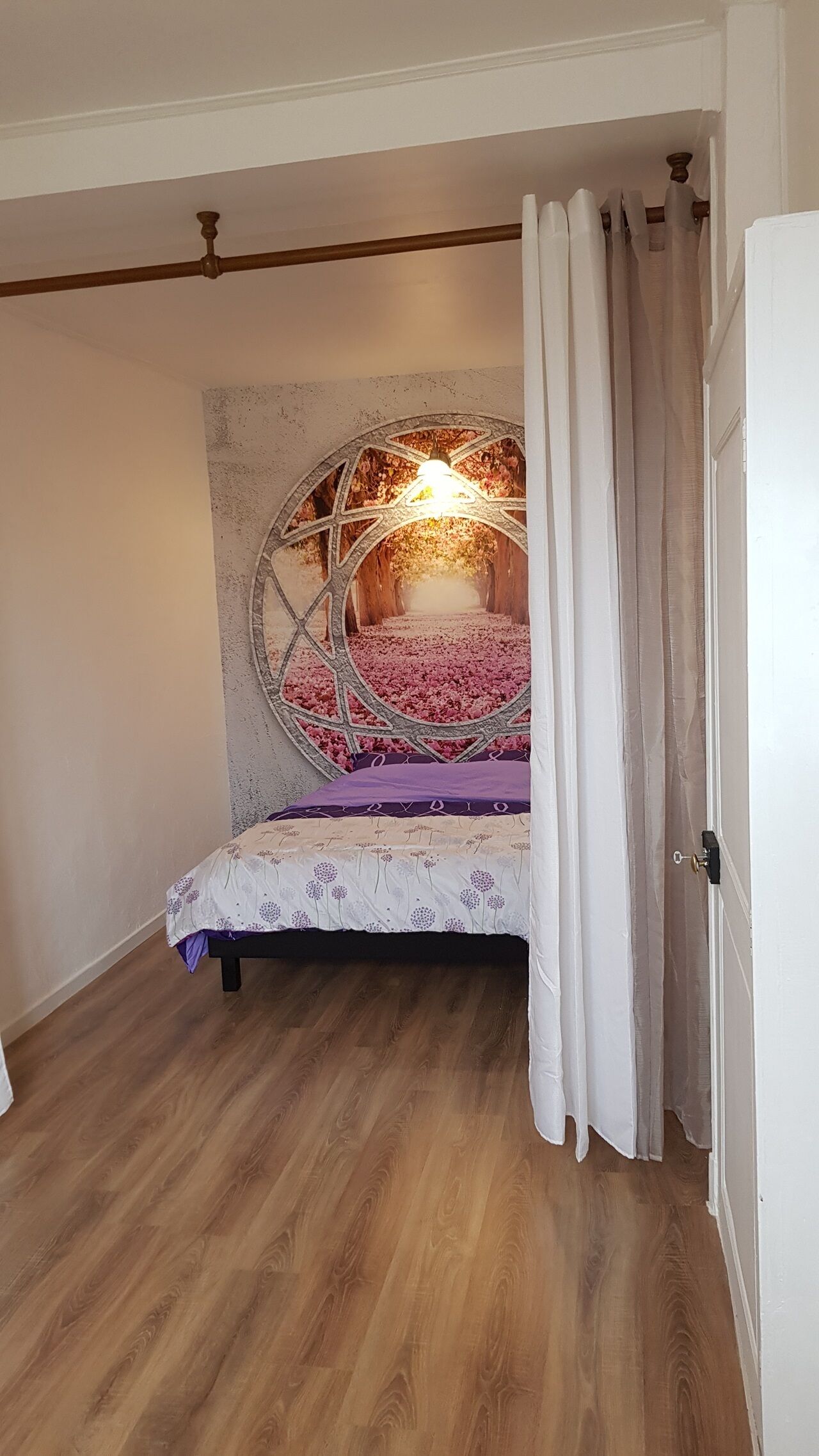 Een slaapkamer met een bed, houten vloer en een decoratieve plafondlamp.