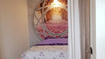 Een slaapkamer met een bed, houten vloer en een decoratieve plafondlamp.