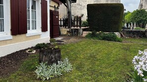 Een traditioneel gebouw met een stenen gevel, een houten hek en een verzorgde tuin met een haag en bloeiende planten.