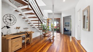 A modern interior with a wooden staircase, a desk with a chair, and a large clock on the wall.