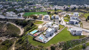 An aerial view of a residential area with modern white buildings, a sports field, and a swimming pool. - Calm and Joy Summer House  (8527+7F4 Afantou, Greece)