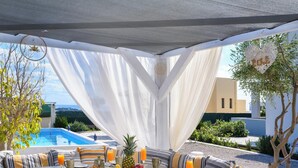 An outdoor dining area with a pool view, featuring a table set with fruits, bread, and drinks, and a cozy seating arrangement. - Calm and Joy Summer House  (8527+7F4 Afantou, Greece)