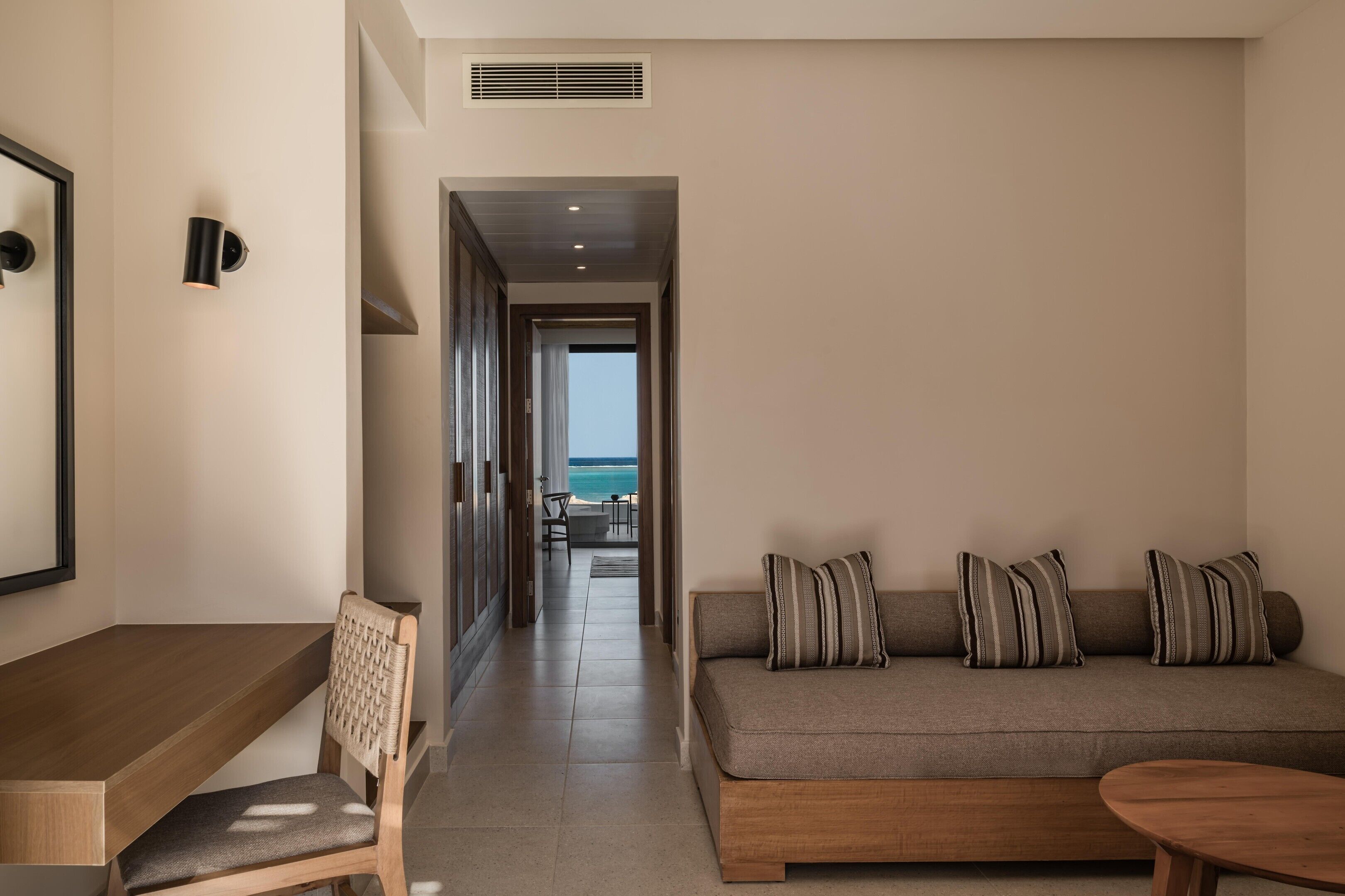 Habitación de hotel moderna con sofá, una mesa de madera, una silla y vista al océano.