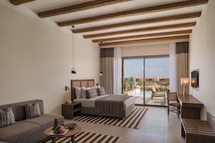 Una habitación de hotel moderna con una cama grande, un sofá, un escritorio y vistas a una piscina y una playa.